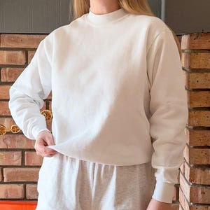May include: A white crew neck sweatshirt with long sleeves. The sweatshirt is made of a soft, comfortable fabric and has a relaxed fit.