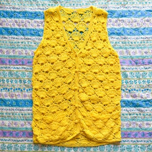 May include: A yellow crocheted vest with a button closure. The vest has a scalloped design and is made of a lightweight yarn.