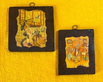 May include: Two framed pictures with a dark brown wooden frame. The picture on the left shows a girl sweeping with a broom. The picture on the right shows a girl in a red dress with a yellow hat standing in a room with a clock on the wall.