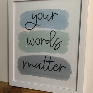 K&ouml;nnte beinhalten: Wei&szlig;er gerahmter Druck mit dem Text "your words matter" in schwarzer kursivschrift auf einem Hintergrund aus drei horizontalen blauen und gr&uuml;nen Aquarellstrichen.