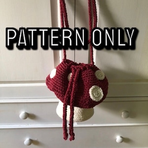 May include: A crocheted mushroom-shaped bag with a red top and white spots and a white stem. The bag has a drawstring closure and a long red strap.