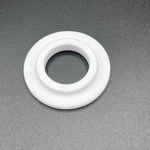 Peut inclure: Un objet blanc et circulaire avec un anneau extérieur surélevé et un trou central. L'objet est fait d'un matériau solide et opaque et repose sur une surface grise. Le design est simple et fonctionnel.