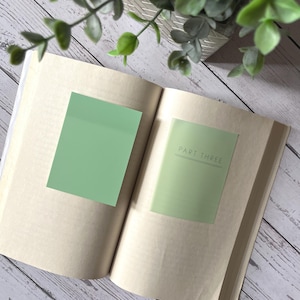 May include: An open book with two green sticky notes. The top note is blank and the bottom note says "PART THREE".