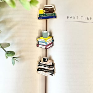 Peut inclure: Trois épingles émaillées sur une page de livre. L'épingle supérieure représente une cafetière et une tasse avec les mots "COFFEE AND BOOKS". L'épingle du milieu a une tasse sur des livres avec "DRINK READ LOVE". L'épingle du bas dit "HAPPINESS IS A CUP OF TEA & A GOOD BOOK."