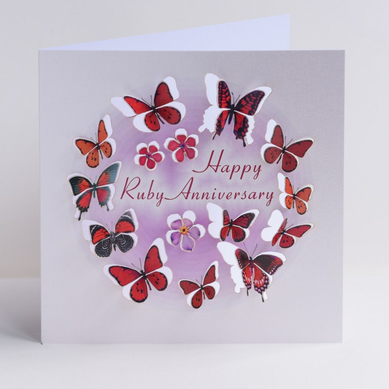 Peut inclure: Une carte de v&oelig;ux avec un fond violet et un cercle de papillons rouges. Le texte "Happy Ruby Anniversary" est &eacute;crit au centre du cercle.