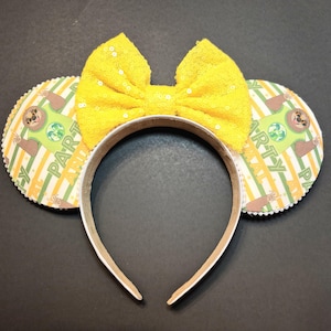 May include: Yellow sequined bow headband with matching ears. The ears feature a sloth graphic with the words "Party Animal" on a striped background. The headband is white.