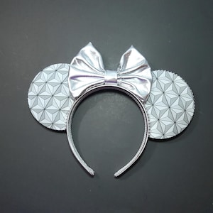 May include: Silver mouse ears headband with a silver bow and a white and gray geometric pattern on the ears.