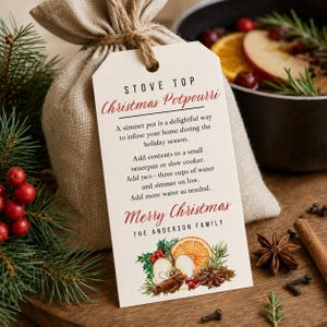Puede incluir: Una bolsa de lino beige con una etiqueta de papel rectangular que muestra el texto STOVE TOP Christmas Potpourri, instrucciones de uso y una ilustración en acuarela de rodajas de naranja, canela, anís estrellado y bayas de acebo.