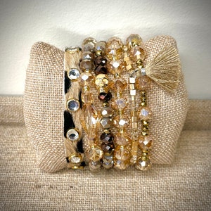 May include: A stack of beaded bracelets in shades of gold, brown, and clear. One bracelet features a black and white animal print with clear rhinestone accents. A gold tassel hangs from one bracelet.