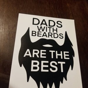 Puede incluir: Gráfico en blanco y negro con una gran silueta de barba. El texto dice "Los papás con barba son los mejores".
