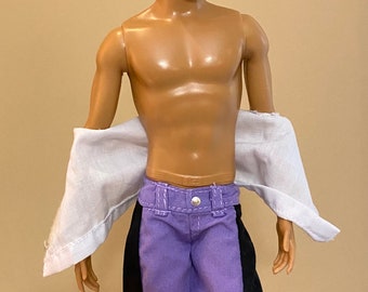 Puede incluir: Una muñeca con cabello castaño y tez bronceada que lleva gafas con montura negra, una camisa blanca y pantalones morados con rayas negras a los lados.