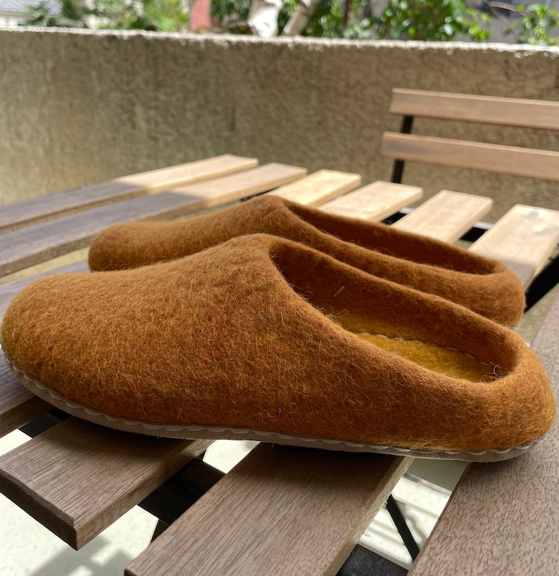 May include: A pair of brown wool slippers with a simple design. The slippers are made of a soft, fuzzy material and have a slightly rounded toe.