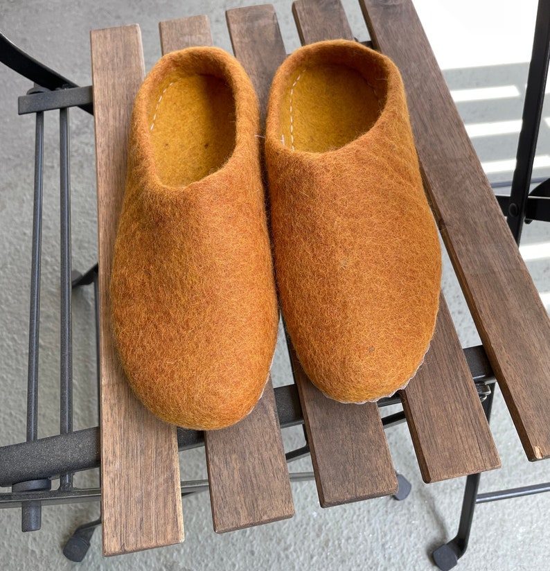 May include: A pair of brown felt slippers with a soft, fuzzy texture. The slippers are sitting on a wooden surface.