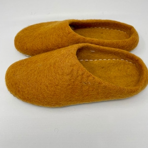 May include: A pair of mustard yellow felt slippers. The slippers are made of a soft, fuzzy material and have a simple, slip-on design.