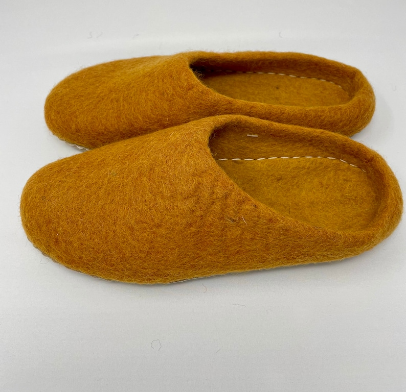 May include: A pair of mustard yellow felt slippers. The slippers are made of a soft, fuzzy material and have a simple, slip-on design.