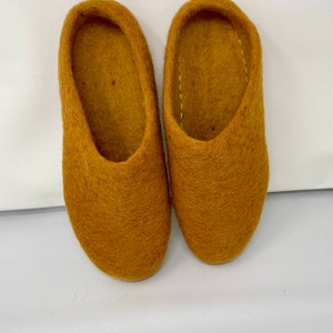 May include: A pair of mustard yellow felt slippers. The slippers are soft and cozy, perfect for keeping your feet warm in the winter.