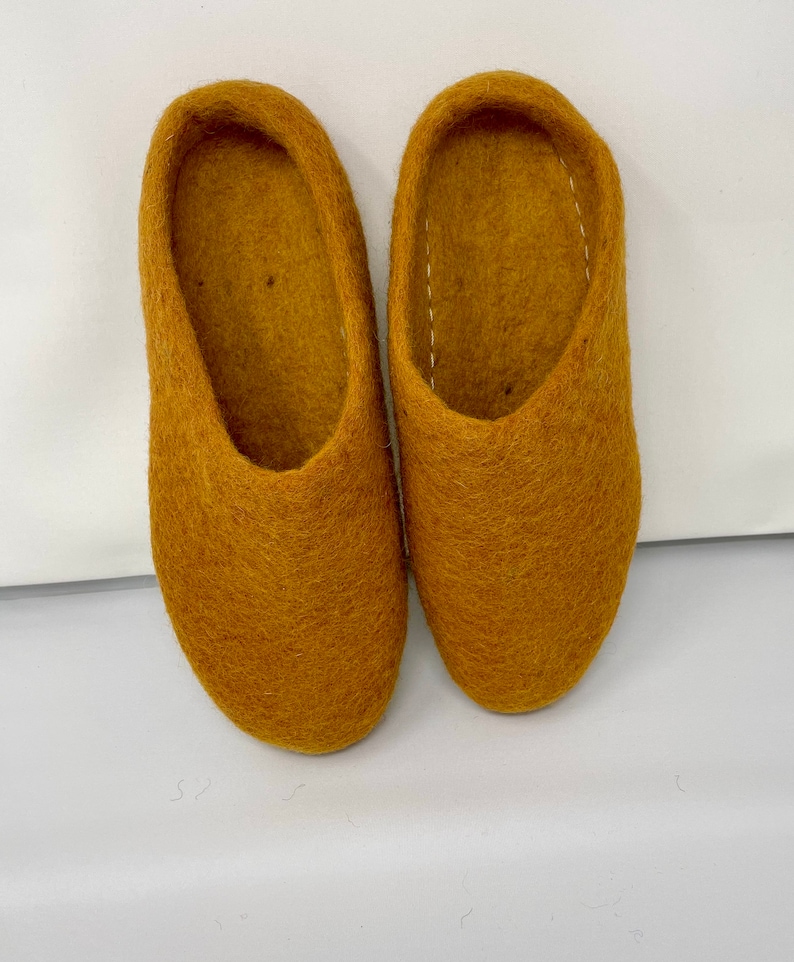 May include: A pair of mustard yellow felt slippers. The slippers are soft and cozy, perfect for keeping your feet warm in the winter.