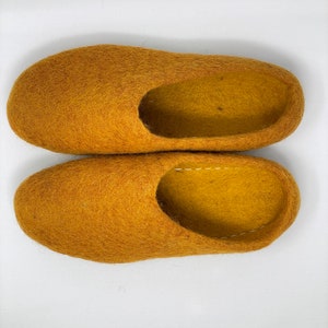May include: A pair of mustard yellow wool slippers. The slippers are made of a soft, fuzzy material and have a simple, rounded shape.