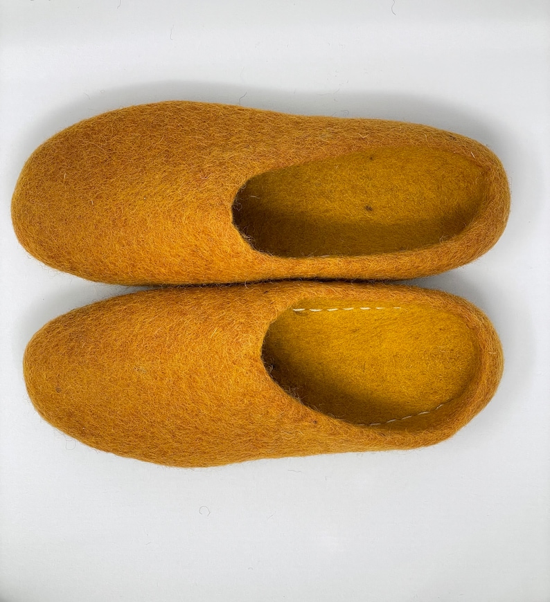 May include: A pair of mustard yellow wool slippers. The slippers are made of a soft, fuzzy material and have a simple, rounded shape.