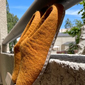 May include: A pair of brown felt slippers with a white trim. The slippers are sitting on a wooden surface.
