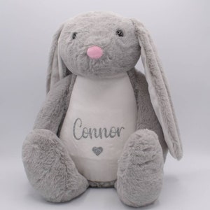 May include: A gray plush bunny with long ears and a white patch on its chest. The patch has the name "Connor" embroidered in silver glitter and a small silver glitter heart.