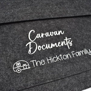 May include: Dark grey felt document holder with the words "Caravan Documents" and "The Hickton Family" printed in white. A white graphic of a caravan is also present. The document holder has a flap closure.