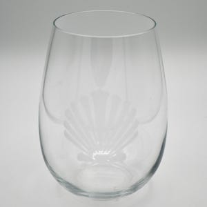 Puede incluir: Una copa de vino de vidrio transparente con una concha grabada en el lateral.