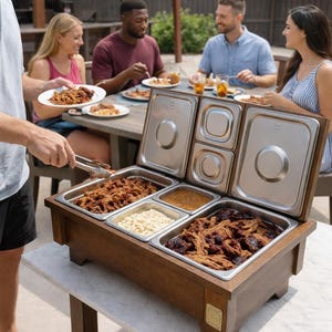 May include: A wooden buffet server with stainless steel food pans, filled with various dishes. The server is on a white marble table, with people seated at a table in the background. The server has a dark wood finish.