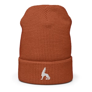 Puede incluir: Un gorro de punto de color óxido con un logotipo de lobo blanco bordado en la parte delantera.