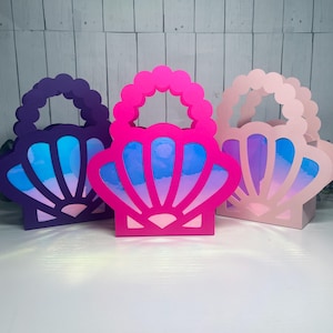 Può includere: Tre sacchetti di carta colorati a forma di conchiglie con accenti blu e viola iridescenti. I sacchetti hanno manici e sono perfetti per bomboniere o regali.