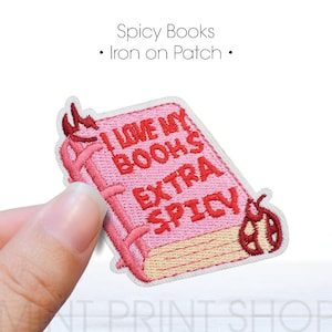 May include: Pink embroidered iron-on patch with the text "I LOVE MY BOOKS EXTRA SPICY". The patch features a book design with red accents and a ladybug. The text "Spicy Books - Iron on Patch" is above the patch.