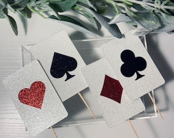 Peut inclure: Quatre toppers de gâteau en forme de carte blanche avec des paillettes. Les toppers présentent un cœur rouge, une pique noire, un trèfle noir et un carreau rouge.