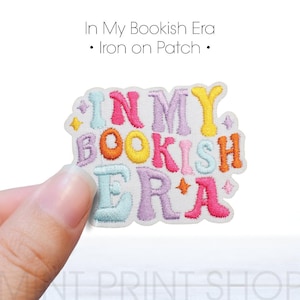 Puede incluir: Un parche bordado multicolor con el texto "In My Bookish Era". El parche presenta las palabras en varios colores, incluyendo rosa, naranja, amarillo y azul. El parche es de tipo termoadhesivo.