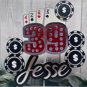 May include: A red and silver glitter cake topper with the number 39, the name "Jesse", playing cards, and poker chips with dollar signs.