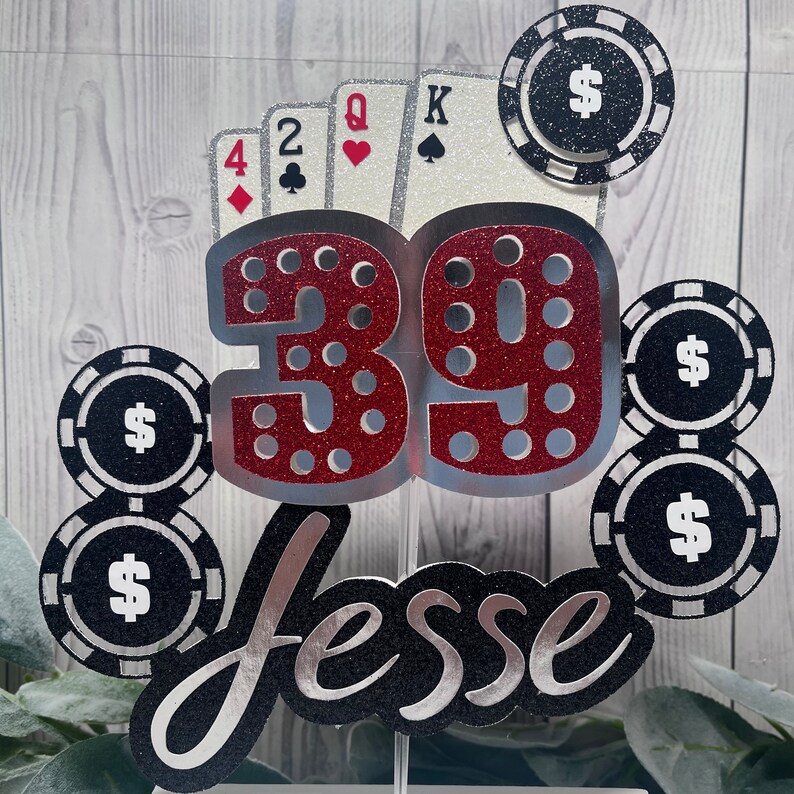 May include: A red and silver glitter cake topper with the number 39, the name "Jesse", playing cards, and poker chips with dollar signs.