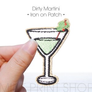 May include: Embroidered patch in the shape of a martini glass, filled with a green liquid and garnished with a green olive and a red stem. The patch has a gold glitter border and the text "Dirty Martini - Iron on Patch".