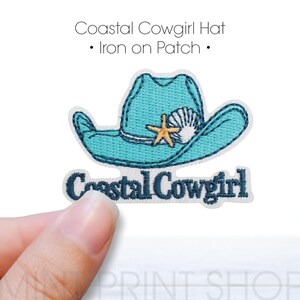 Puede incluir: Un parche bordado con un sombrero de vaquero turquesa con un diseño de concha y estrella de mar. El texto "Coastal Cowgirl" está debajo del sombrero. El parche es para planchar.