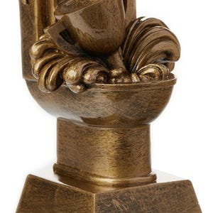 Puede incluir: Un trofeo de color dorado con forma de inodoro con una copa encima. El trofeo tiene un diseño detallado con una base de pedestal y un inodoro. La tapa del inodoro está levantada y la copa está inclinada.