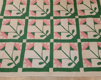 May include: A green and pink patchwork quilt with a floral design. The quilt is made up of squares with a repeating pattern of green leaves and pink flowers.