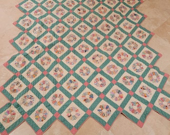May include: A large, handmade quilt with a pattern of pink and green squares. Each square features a circular design made of colorful fabric scraps.