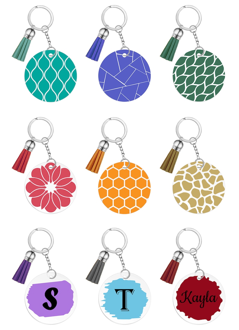 May include: A collection of keychains with silver rings and tassel accents. The round pendants feature various designs, including geometric patterns, floral motifs, and personalized text. Colors include teal, blue, green, red, orange, and brown.