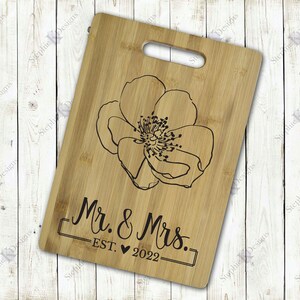 May include: A wooden cutting board with a floral design and the text "Mr. & Mrs. EST. 2022" engraved on it.