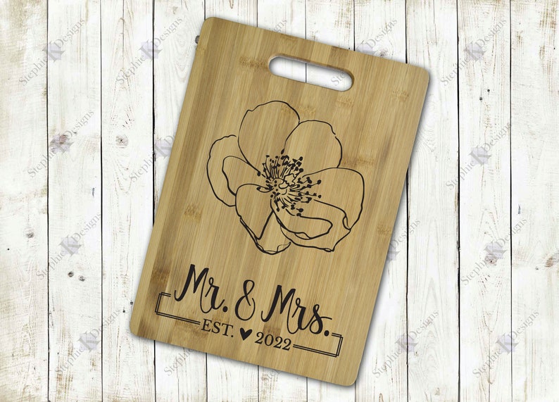 May include: A wooden cutting board with a floral design and the text "Mr. & Mrs. EST. 2022" engraved on it.