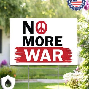 May include: A white sign with the words "NO MORE WAR" in black and red. The word "NO" has a peace symbol in place of the letter "O". The sign is in a yard with a house and greenery in the background.