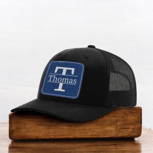 May include: Black trucker hat with a blue and white patch that says "T Thomas" on it.