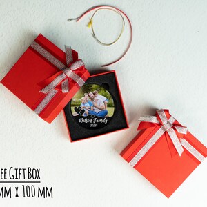 May include: A black circular ornament with a photo of a family of four. The ornament is in a red gift box with a white ribbon. The text "Wilson Family 2024" is printed on the ornament.