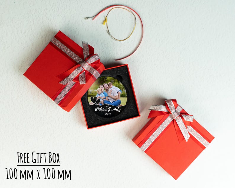 May include: A black circular ornament with a photo of a family of four. The ornament is in a red gift box with a white ribbon. The text "Wilson Family 2024" is printed on the ornament.