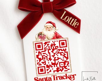 Könnte beinhalten: Weißer Weihnachtsschmuck mit rotem QR-Code und den Worten "Santa Tracker". Der Schmuck zeigt eine Illustration des Weihnachtsmanns und ist mit einer roten Samtschleife versehen. Der Name "Lottie" ist auf der Schleife aufgedruckt.