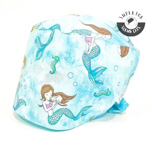 May include: A blue scrub cap with a mermaid and seahorse pattern. The cap has a tie on the back and says "Superior Scrub Caps" in black text.