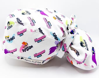 Könnte beinhalten: Weiße OP-Mütze mit einem sich wiederholenden Muster der Powerpuff Girls-Charaktere und -Logos. Die Mütze hat einen Bindeverschluss an der Rückseite.